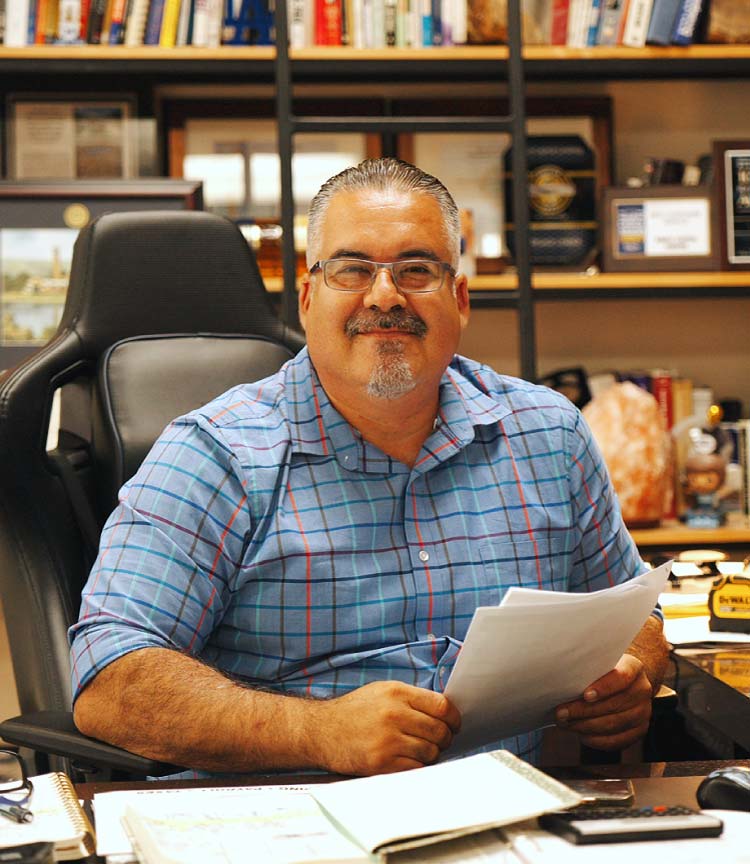 Aldo Gutierrez, President and Owner of Direct Capital Lending, smiling at his office desk while holding mortgage loan documents, representing experienced and trusted home financing services.