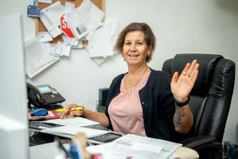 A friendly team member at Direct Capital Lending smiling and waving from her office desk, showcasing the welcoming and client-first atmosphere of the brokerage.