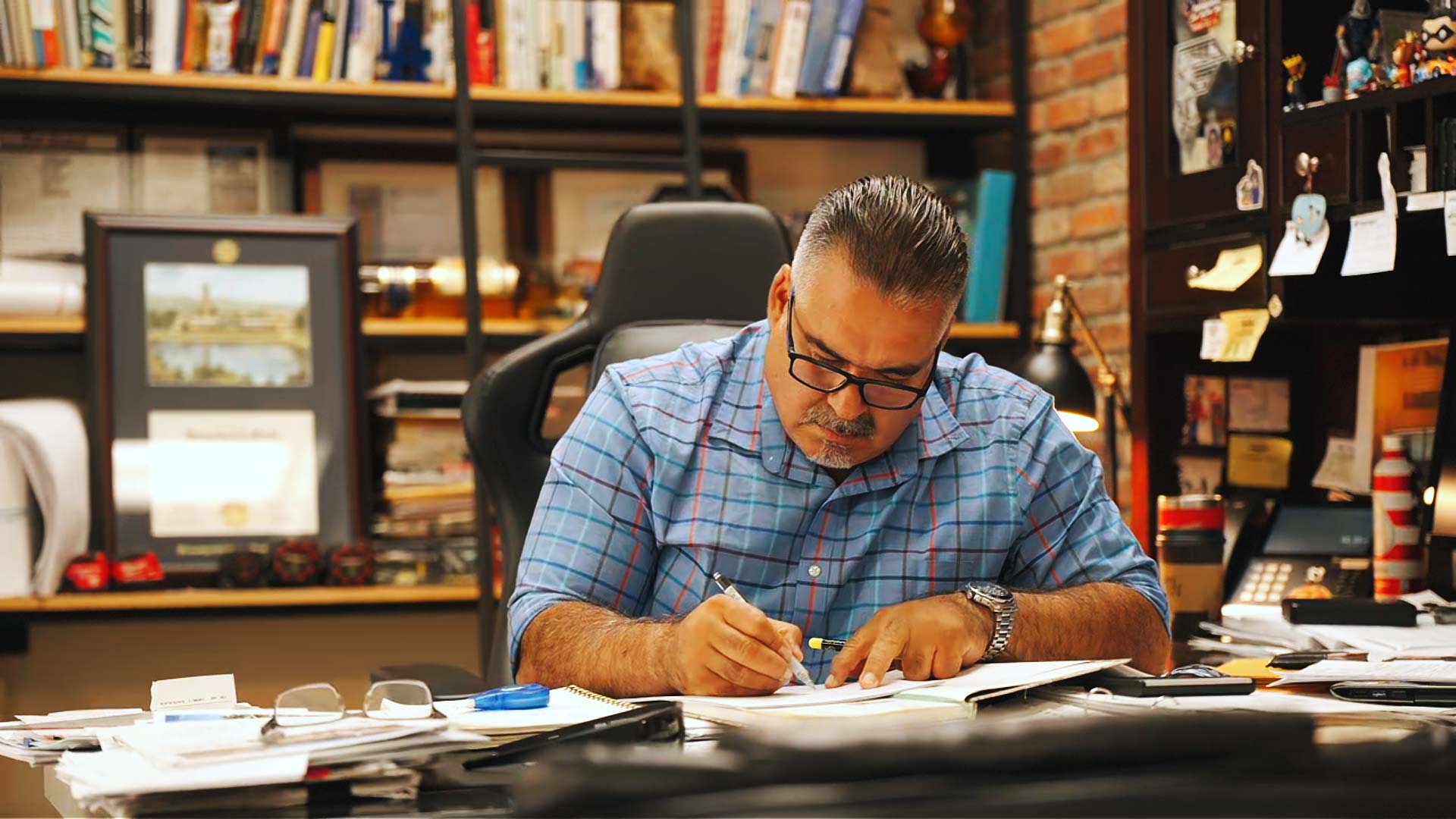 Aldo Gutierrez, Real Estate Finance Specialist, carefully reviewing loan applications and mortgage paperwork at his office desk.